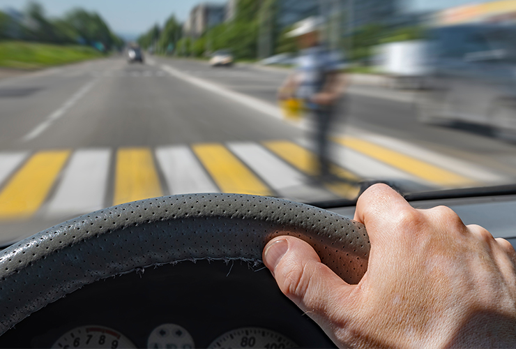 The,Driver,Hand,On,The,Steering,Wheel,Of,A,Car the driver hand on the steering wheel of a car moving at high speed and passing a pedestrian crossing with the risk of hitting a person